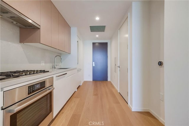 kitchen with visible vents, a sink, stainless steel appliances, light wood-style floors, and under cabinet range hood