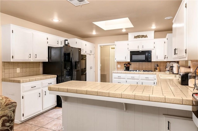 kitchen with white cabinetry, kitchen peninsula, tile counters, and black appliances