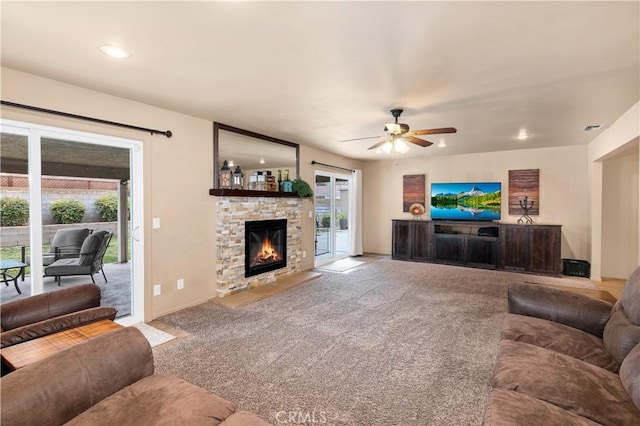 living room with a stone fireplace, light colored carpet, and ceiling fan