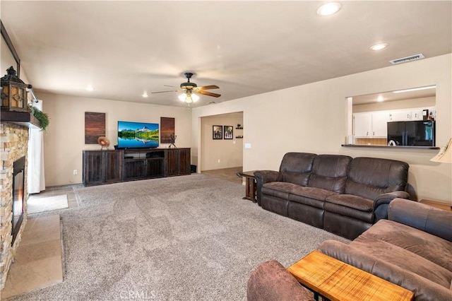 living room featuring a stone fireplace, light carpet, and ceiling fan