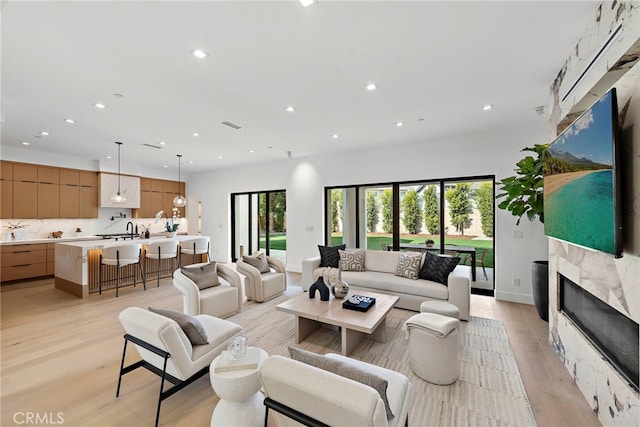 living room with a high end fireplace, sink, and light hardwood / wood-style floors