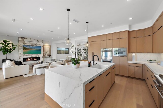 kitchen with a large island, sink, hanging light fixtures, light wood-type flooring, and a fireplace