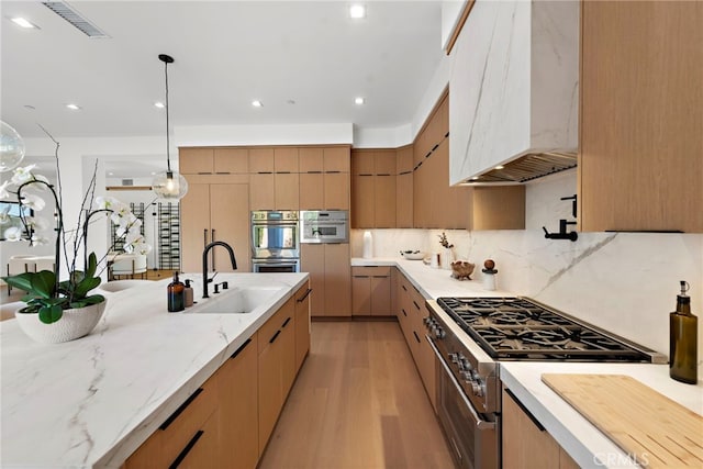 kitchen with premium range hood, decorative light fixtures, sink, stainless steel appliances, and light wood-type flooring