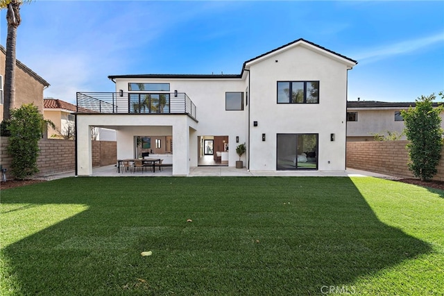 rear view of house with a balcony, a lawn, and a patio area