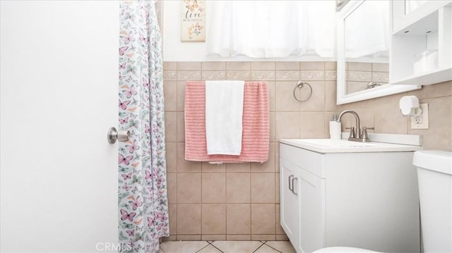 bathroom featuring toilet, tile patterned floors, tile walls, and vanity