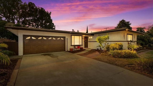 view of front of property featuring driveway, fence, an attached garage, and stucco siding