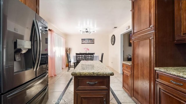 kitchen with light tile patterned floors, stainless steel fridge, light stone counters, and a center island