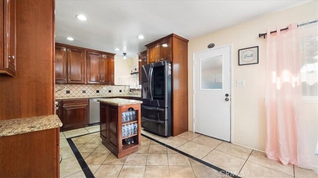 kitchen with light tile patterned floors, appliances with stainless steel finishes, backsplash, light stone countertops, and a kitchen island