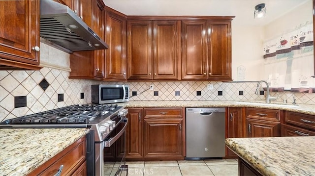 kitchen with decorative backsplash, appliances with stainless steel finishes, light stone counters, range hood, and a sink