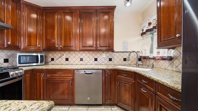 kitchen featuring stainless steel appliances, light stone counters, backsplash, and a sink