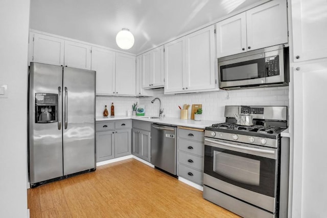 kitchen with appliances with stainless steel finishes, tasteful backsplash, white cabinetry, sink, and light hardwood / wood-style flooring