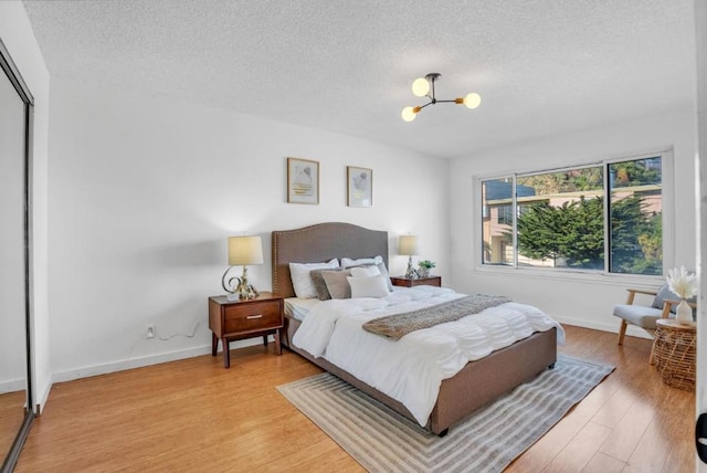 bedroom with an inviting chandelier, a textured ceiling, light hardwood / wood-style floors, and a closet