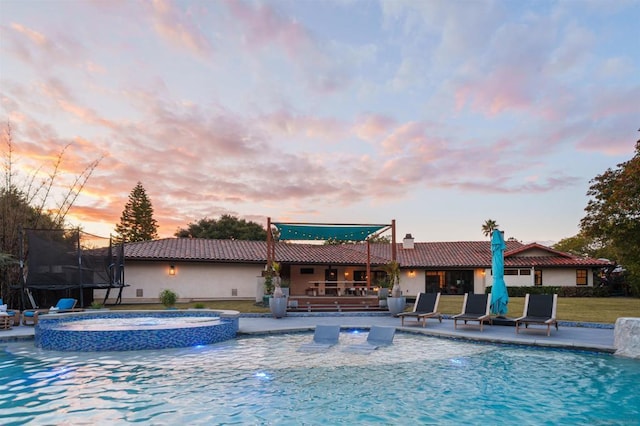 pool at dusk with a trampoline, a patio, and an in ground hot tub