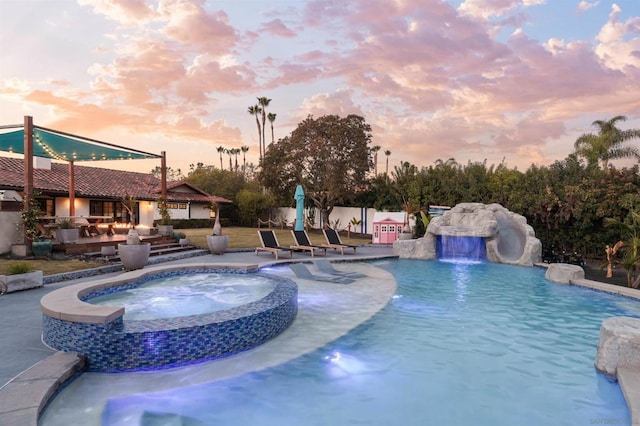 pool at dusk with a patio, pool water feature, and an in ground hot tub