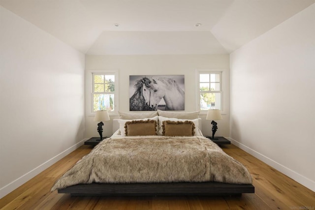 bedroom with multiple windows, vaulted ceiling, and hardwood / wood-style flooring