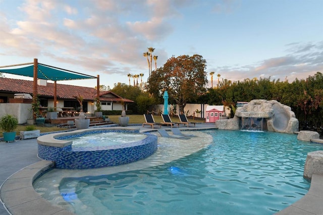 pool at dusk with an in ground hot tub and pool water feature