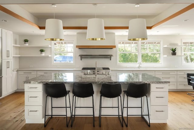 kitchen featuring stone counters, white cabinetry, stove, and a kitchen island with sink