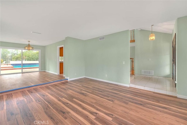 spare room featuring lofted ceiling, hardwood / wood-style floors, and a notable chandelier