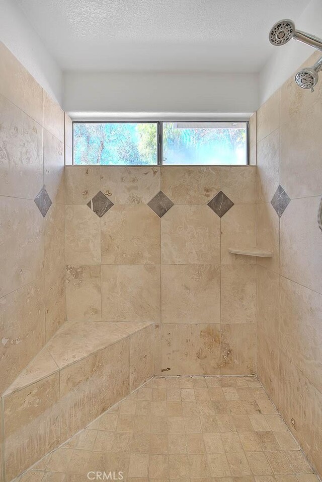 bathroom with a tile shower, a textured ceiling, and a healthy amount of sunlight