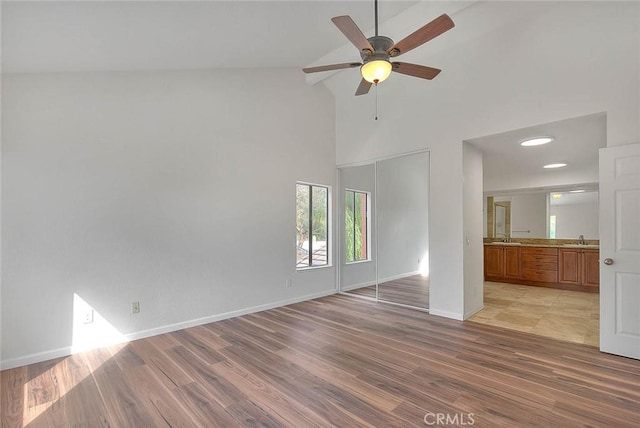 unfurnished room with sink, light hardwood / wood-style floors, high vaulted ceiling, and ceiling fan