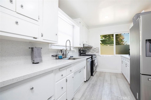 kitchen featuring sink, appliances with stainless steel finishes, tasteful backsplash, light stone countertops, and white cabinets