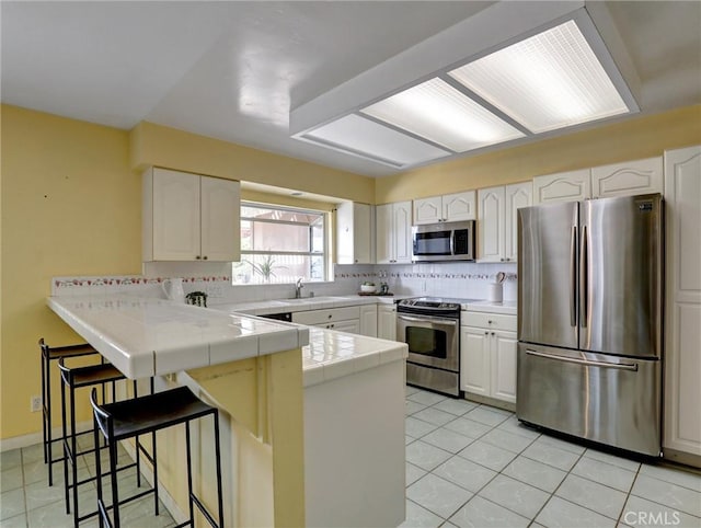 kitchen with appliances with stainless steel finishes, tile counters, kitchen peninsula, and white cabinets