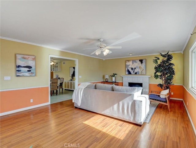 living room with crown molding, ceiling fan, a fireplace, and light hardwood / wood-style floors