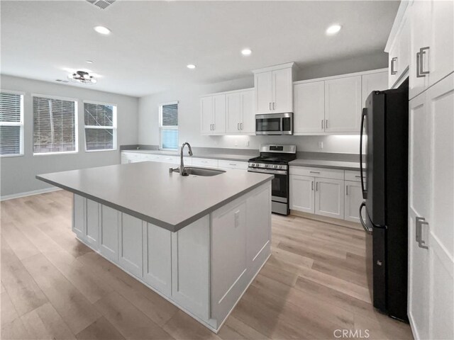 kitchen with an island with sink, sink, white cabinets, light hardwood / wood-style floors, and stainless steel appliances