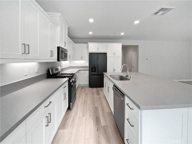 kitchen featuring sink, a center island with sink, stainless steel appliances, light hardwood / wood-style floors, and white cabinets