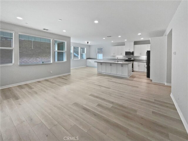 kitchen with sink, white cabinets, stainless steel appliances, a center island with sink, and light wood-type flooring