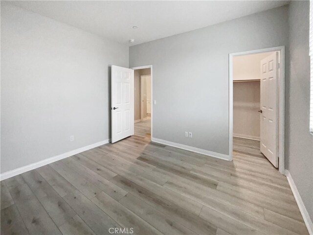 unfurnished bedroom with a spacious closet, light hardwood / wood-style flooring, and a closet