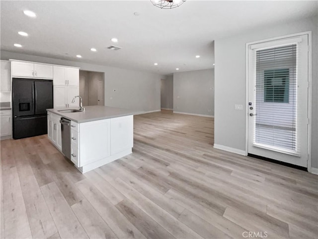 kitchen featuring sink, black fridge, light hardwood / wood-style flooring, an island with sink, and white cabinets