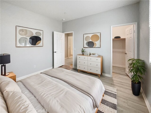 bedroom featuring a walk in closet and light hardwood / wood-style flooring