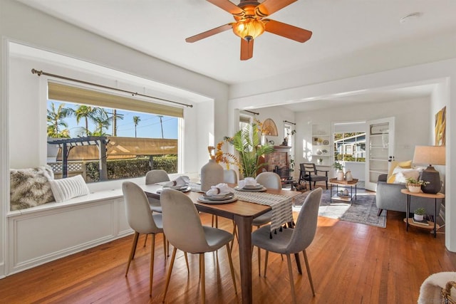 dining area with ceiling fan, a brick fireplace, hardwood / wood-style floors, and built in features