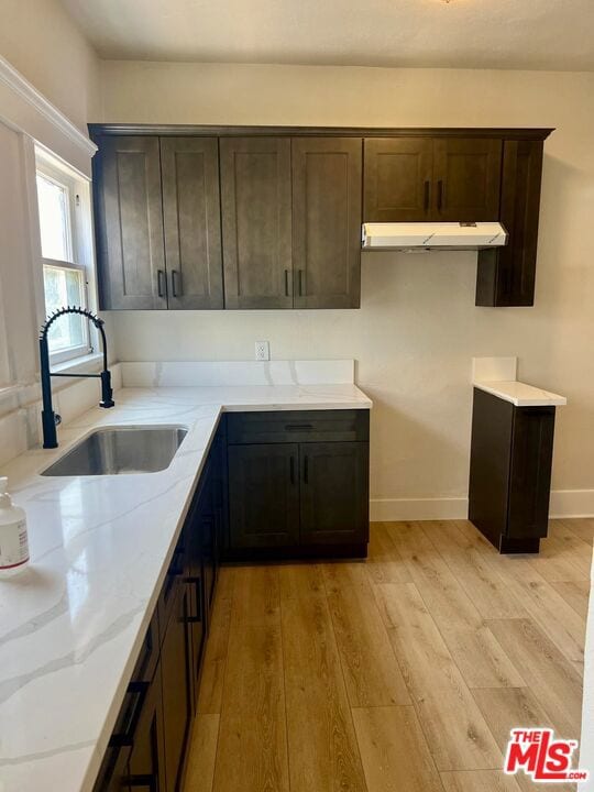 kitchen with sink, dark brown cabinets, light stone countertops, and light wood-type flooring