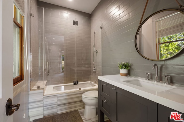 full bathroom featuring toilet, bath / shower combo with glass door, tile walls, vanity, and backsplash