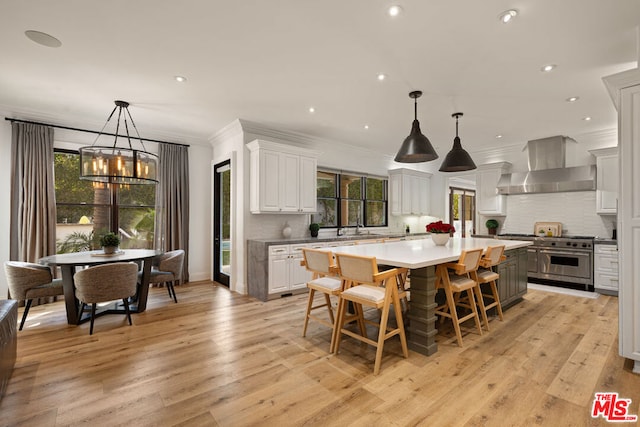 kitchen featuring wall chimney exhaust hood, hanging light fixtures, a kitchen island, and white cabinets