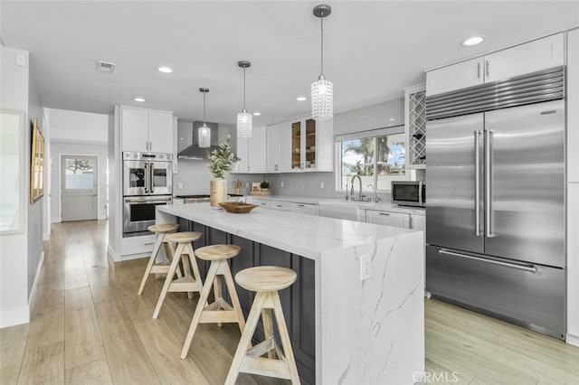 kitchen featuring sink, appliances with stainless steel finishes, a center island, white cabinets, and wall chimney exhaust hood