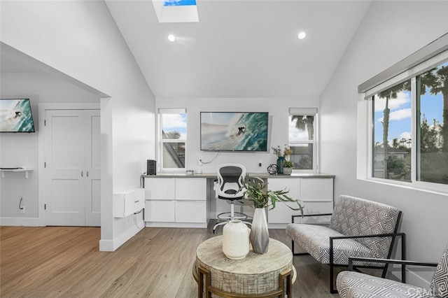 living area featuring a skylight, plenty of natural light, high vaulted ceiling, and light hardwood / wood-style flooring