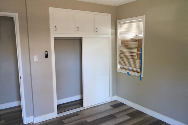 unfurnished bedroom with a closet, baseboards, and dark wood finished floors