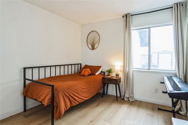 bedroom with multiple windows, light wood-type flooring, and baseboards