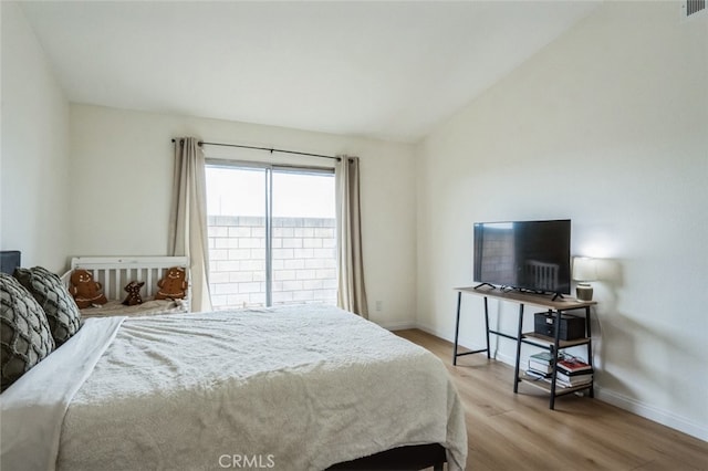 bedroom featuring baseboards, wood finished floors, and lofted ceiling
