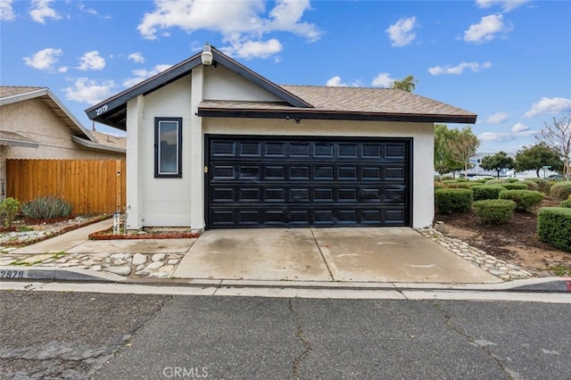 view of front facade featuring fence, stucco siding, an attached garage, and driveway