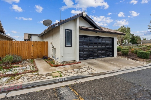 exterior space featuring a garage, driveway, fence, and stucco siding