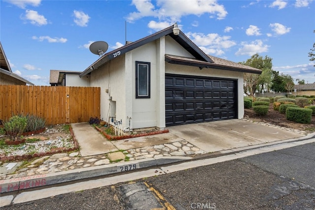 view of home's exterior with an attached garage, fence, driveway, and stucco siding