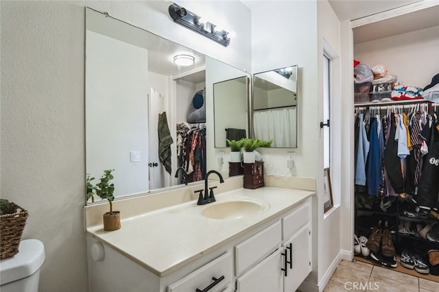 bathroom with toilet, a walk in closet, vanity, and tile patterned floors