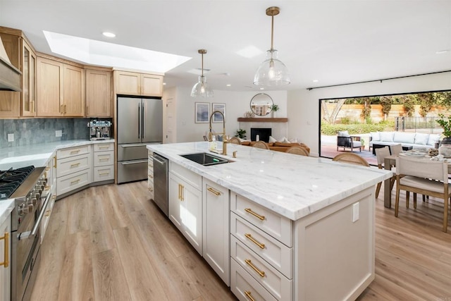 kitchen with pendant lighting, sink, backsplash, a kitchen island with sink, and stainless steel appliances