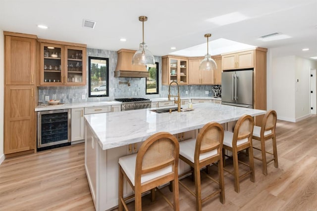 kitchen with premium range hood, sink, high end appliances, an island with sink, and beverage cooler