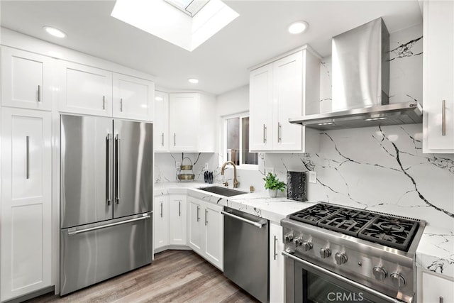 kitchen with sink, high end appliances, light stone counters, wall chimney range hood, and white cabinets