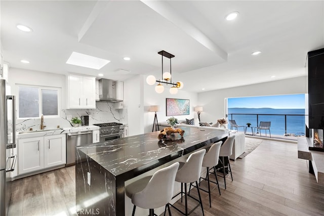 kitchen with wall chimney range hood, white cabinetry, a center island, high quality appliances, and a water view